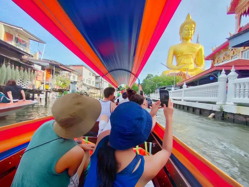 Monks in orange robes on a small boat receiving morning alms from a canal-side wooden house in Thonburi Bangkok