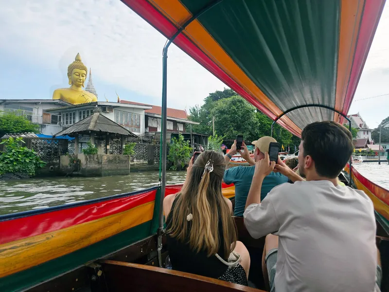 Long boat on a Bangkok canal surrounded by tropical trees and wooden buildings in the Thonburi west bank district on a bangkok canal tour