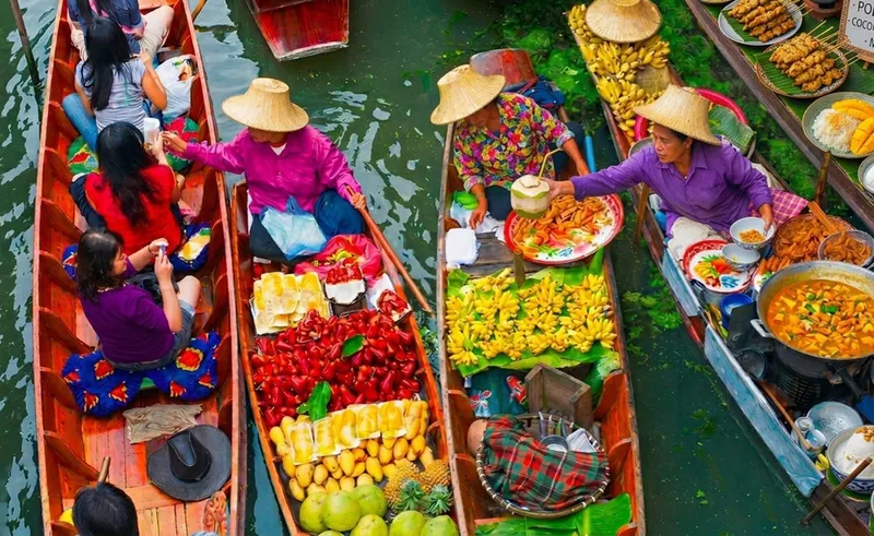Tourists on a flat-bottomed boat cruising through Damnoen Saduak Floating Market with colourful vendor boats on a bangkok boat tour day trip